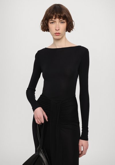 Bodysuit negro de manga larga con escote barco y textura recogida en la cintura. Tela suave y elástica. Acentuado con un bolso negro de mano.