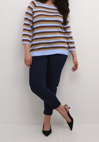 Pasiasty sweter w jasnoniebieskim, brązowym i kremowym kolorze, z rękawami do trzech kwartałów, w połączeniu z granatowymi dopasowanymi spodniami i czarnymi szpilkami.