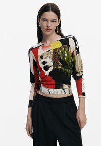 Top lavorato a maglia multicolore con motivi grafici, tra cui volti e foglie, con maniche lunghe e scollatura rotonda. Abbinato a pantaloni neri.