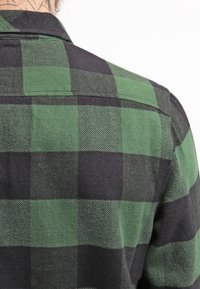 Rutigt skjorta i gröna och svarta nyanser. Har ett texturerat tyg med ett traditionellt rutmönster och en klassisk krage.