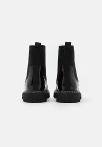 Czarne lakierowane botki za kostkę z elastycznymi panelami bocznymi, masywnymi czarnymi gumowymi podeszwami i gładką, błyszczącą powłoką.