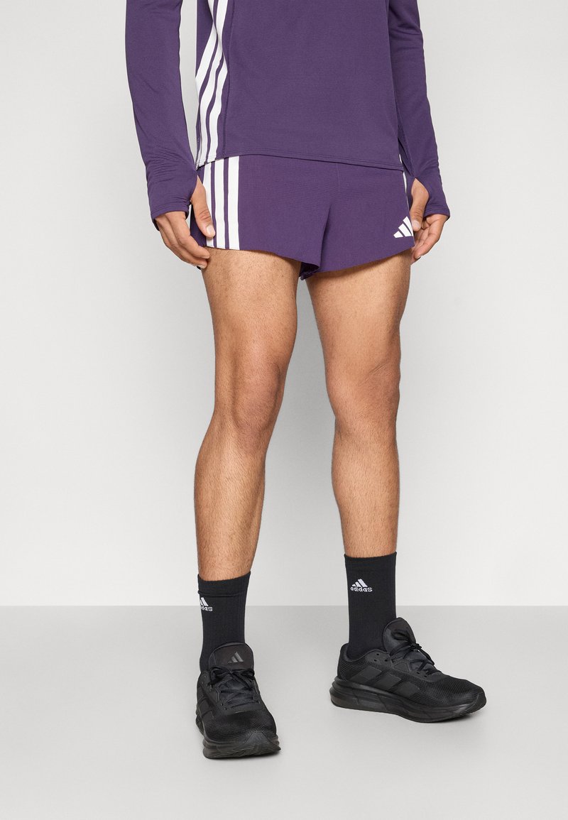 Μωβ αθλητικό μακρυμάνικο τοπ με λευκές ρίγες, ταιριαστά μωβ σορτς, μαύρες κάλτσες αστραγάλου και μαύρα αθλητικά παπούτσια.