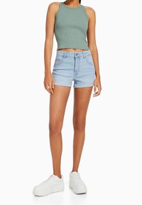 Top corto verde a righe, pantaloni corti di jeans chiari e sneakers bianche con plateau. I pantaloni corti hanno un design aderente. Texture liscia e stile casual.