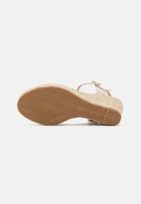 Wedge sandal with a woven jute platform and rubber sole. Pale pink strap with a buckle. Textured sole for grip.