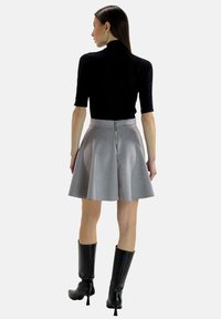 Schwarzes Oberteil mit kurzen Ärmeln und einem grauen schwingenden Rock mit einem Reißverschluss hinten. Das Modell trägt knielange schwarze Stiefel. Glattes Material.