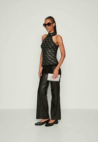 Woman wearing black sleeveless patterned top, black leather wide-leg pants, black flats, holding white clutch, and black sunglasses.