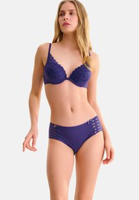 Ensemble de lingerie violet composé d'un soutien-gorge à motif texturé à carreaux et de bas taille haute à côtes. Les détails notables incluent des bords en scalloped et des sangles sur les côtés.