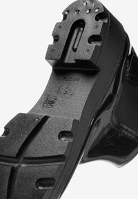 Semelle de chaussure noire avec de profonds reliefs et une texture adhérente, portant les marquages « 6 » et « Fabriqué en Chine ». 