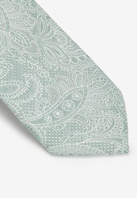 Lys mintgrøn slips i struktureret stof, med indviklede hvide blomster- og paisley mønstre, afsluttet med en spids spids.