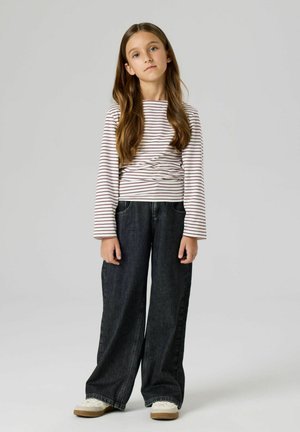 Długi rękaw, bluzka w paski w kolorze białym i bordowym, zestawiona z szerokimi ciemnymi dżinsami oraz lekkimi sneakersami z teksturowaną podeszwą.