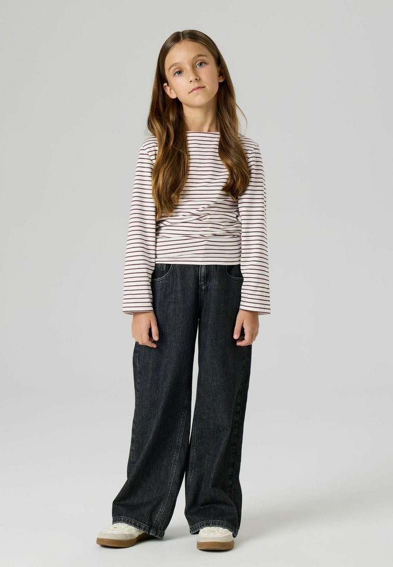 Długi rękaw, bluzka w paski w kolorze białym i bordowym, zestawiona z szerokimi ciemnymi dżinsami oraz lekkimi sneakersami z teksturowaną podeszwą.