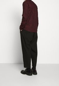 Camicia rossa a maniche lunghe con texture, pantaloni neri a vestibilità ampia e scarpe nere con accenti rossi, viste da dietro. Design semplice e moderno.