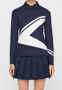 Marinblå pikétröja med lång ärm och vit diagonal randdesign samt klassisk krage, kombinerad med en marinblå plisserad kjol. Tyg av bomullsblandning.