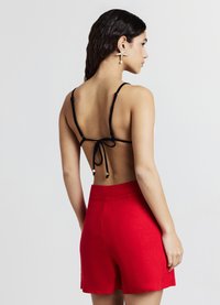 Schwarzes rückenfreies Top mit dünnen Trägern, die hinten gebunden sind, kombiniert mit hochgeschnittenen roten Shorts. Glatte Textur und lebendige Farben.