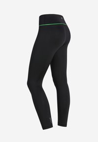 Leggings athletici neri con accento verde in vita, design a vita alta, realizzati in tessuto elastico, con dettaglio del logo vicino alla caviglia.