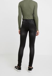 Vaqueros ajustados negros hechos de denim, con cintura alta, trabillas para cinturón y textura suave. Combinados con zapatillas negras.