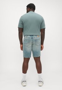 Shorts in denim blu chiaro con un lavaggio sbiadito, tasche posteriori e una linea dritta. Abbinati a una maglietta a maniche corte di colore teal.
