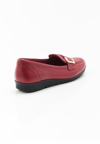 Scarpa slip-on in pelle rossa con suola piatta nera. Presenta una fibbia in tono oro e una cintura testurizzata. Finitura liscia con punta arrotondata.