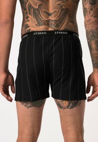 Zwarte boxershorts van stof met witte verticale streepjes. Voorzien van een elastische tailleband met het logo "JP1880". Soepele textuur.