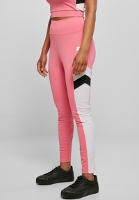 Rosa treningsbukser med svart og hvit chevronmønster, tettsittende, høy midje og elastisk materiale. Kombinert med svarte joggesko.