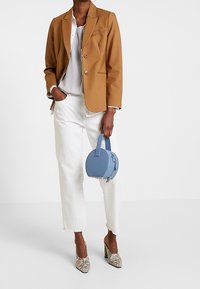 Brun kavaj med två knappar, randig skjorta under, vita cropped-byxor, blå cirkelformad handväska och mönstrade klackar.