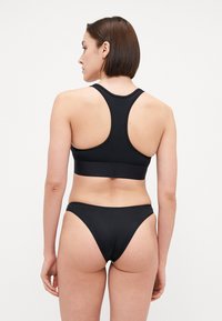 Zwarte sportbeha met een racerbackontwerp en brede band; gecombineerd met bijpassende hooggesneden bikini-broekjes. Soepele, rekbare stof.