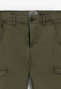 Pantalones de algodón verde oliva con cierre frontal de botón, dos bolsillos laterales y tejido texturizado. Presenta una etiqueta en la cintura.