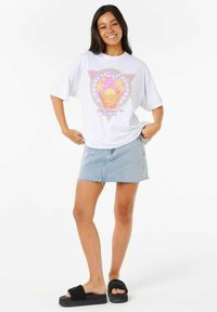 Hvid oversized t-shirt med et farverigt grafisk design, lyseblå denimnederdel og sorte platform sandaler. Glatte teksturer og afslappet pasform.