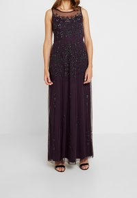 Sleeveless dark purple gown with black floral bead embellishments, sheer neckline, and floor-length skirt, paired with black open-toe heels.