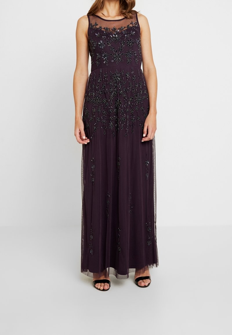 Sleeveless dark purple gown with black floral bead embellishments, sheer neckline, and floor-length skirt, paired with black open-toe heels.
