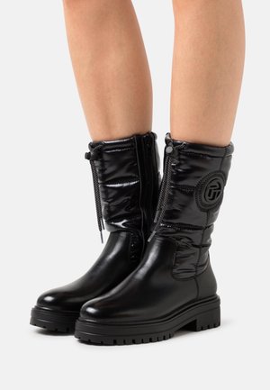 Botas negras acolchadas hasta la rodilla con un acabado brillante, que cuentan con un cierre de cordones en la parte delantera, cierre de cremallera y un detalle de logo texturizado en el costado.