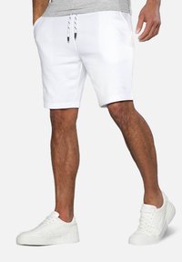 Hvide sportsshort med elastisk talje og snor, med sidelommer og en glat tekstur. Matcher med hvide sneakers.