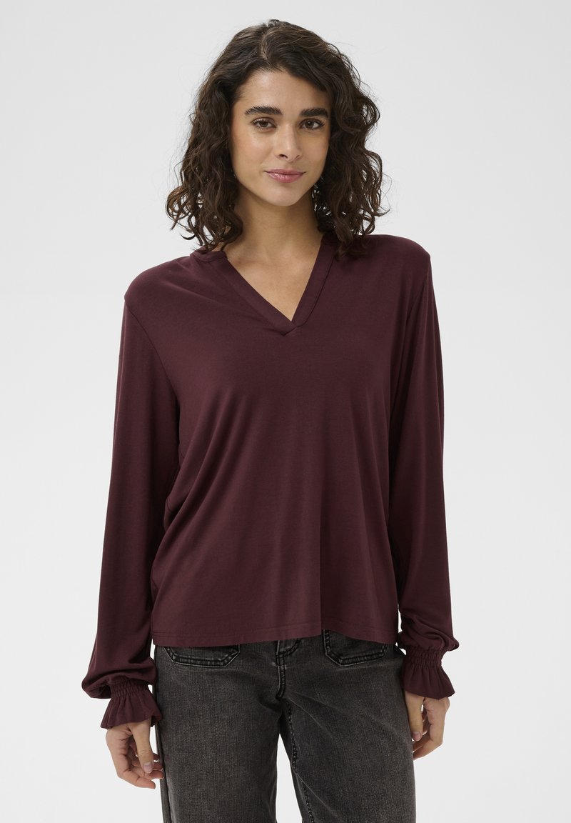 Vínový top s dlouhými rukávy a výstřihem do V, z jemné látky, s nařasenými manžetami a volnějším střihem, doplněný tmavě šedými džíny.