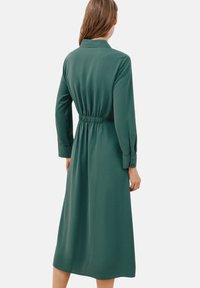 Zelené midi šaty vyrobené z měkké tkaniny, s límečkem, dlouhými rukávy, elastickým pasem a knoflíkovými manžetami.