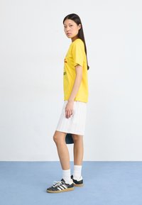 Yellow cotton t-shirt with printed graphics, paired with a white pinstriped skirt. Black and white athletic shoes and white socks complete the look.