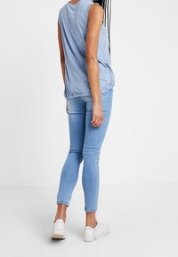 Ljusblå ärmlös topp med små vita prickar, samlad nederkant, i kombination med figurnära ljusblå jeans och vita sneakers.