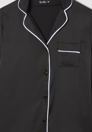 Top in satin nero con piping bianco lungo il colletto, il bordo della tasca e la fila di bottoni; presenta una tasca sul petto e bottoni neri.