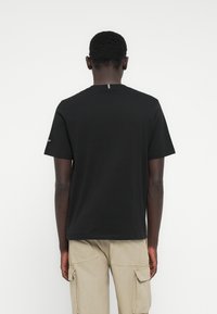 Μαύρο βαμβακερό μπλουζάκι με κοντά μανίκια, στρογγυλή λαιμόκοψη και μικρή γκρι λεπτομέρεια στην πλάτη. Φορεμένο με μπεζ παντελόνι cargo.