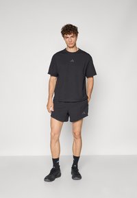 Ensemble de sport noir comprenant un t-shirt à manches courtes et un short. Le matériau est lisse, avec un discret logo sur les deux pièces.