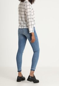 Blusa a scacchi bianchi e neri, maniche lunghe, abbinata a jeans skinny blu e scarpe con piattaforma nere. Orlo visibilmente sfilacciato sui jeans.