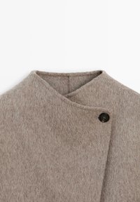 Jasnoszara wełniana płaszcz o teksturowanym wykończeniu, z projektowaniem typu wrap i pojedynczym czarnym zapięciem na guzik przy kołnierzu.