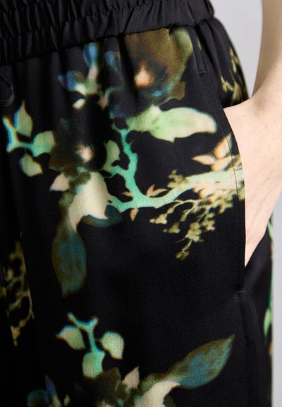 Sort stof med et blomsterdesign i grøn, brun og teal. Har en elastisk talje og sidelomme. Glat overflade.