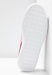 Semelle blanche de sneaker Puma avec motif étoilé, inclinée contre un mur blanc d’angle, montrant l’adhérence texturée et le détail du logo.