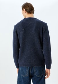 Dunkelblauer Strickpullover mit strukturiertem Rippmuster, das braune Sprenkel aufweist. Lange Ärmel und Rundhalsausschnitt.