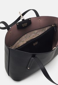Borsa nera con textura e interno marrone chiaro. Dotata di una tasca con zip e accessori in oro. Etichetta del marchio visibile all'interno.