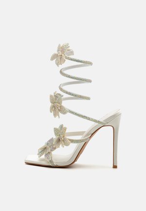 Bela sandala na visokom petu z spiralnim trakama, ukrašena cvetovima i iridescentnim rhinestones. Tekstuirana tkanina sa kvadratnim prstima.
