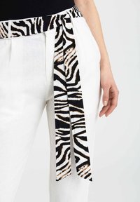 Białe spodnie z czarno-białym paskiem w zebrę zawiązanym w talii, o gładkiej fakturze i kontrastowych wzorach.