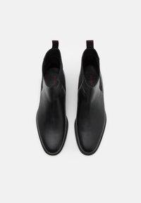 Bottes cheville en cuir noir à texture lisse, bout arrondi et panneaux élastiques latéraux, avec une languette rouge au talon.