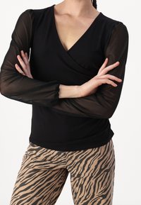 Top nero avvolgente con maniche a sbuffo trasparenti, abbinato a pantaloni beige a strisce zebra. Il top presenta un design scollato a V profonda e una texture morbida.