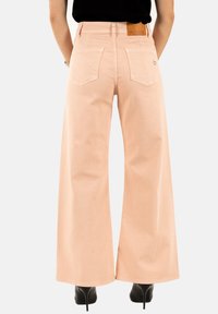 Pantalones de pierna ancha en un tejido texturizado de color rosa pálido, con dos bolsillos traseros y una etiqueta de cuero con la palabra "PLEASE". Combinados con tacones negros.